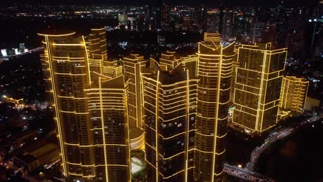 aerial drone footage of the rockwell center skyscrapers in makati, metro manila, glowing with lights at night and surrounded by the vibrant energy of the city skyline.