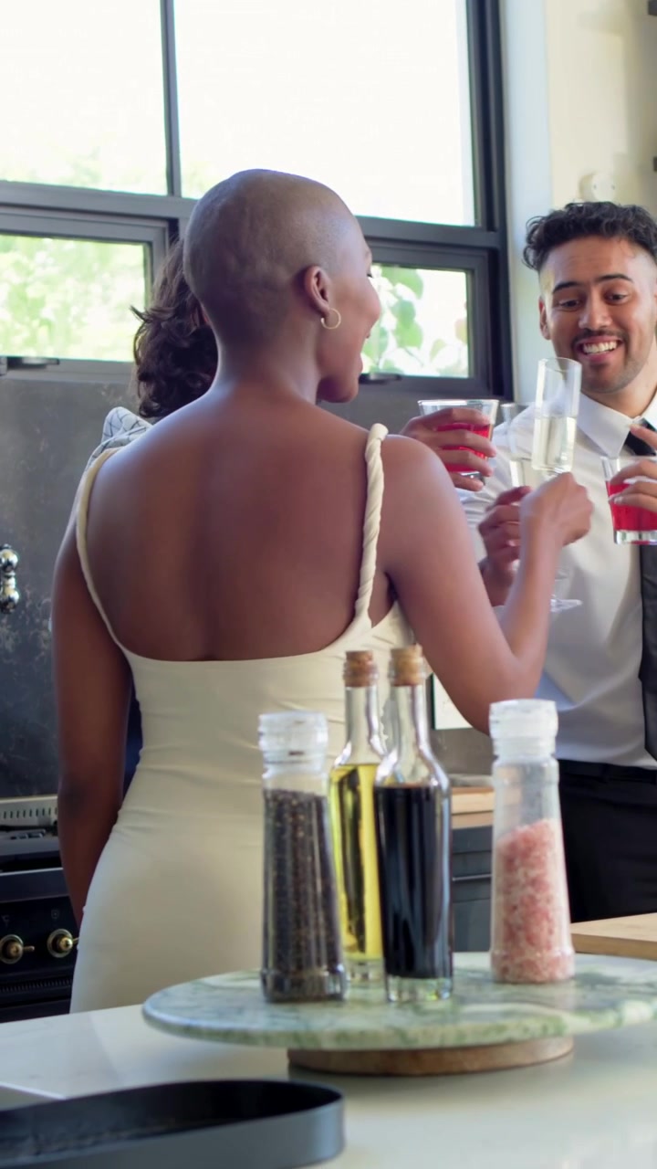 Vertical video: Entering man in tie offering red drink at kitchen island, friends toasting