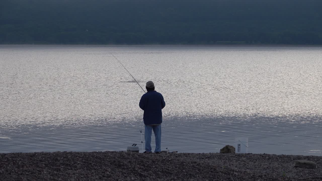 Seorang Pria Memancing di Tepi Danau yang Tenang Saat Fajar