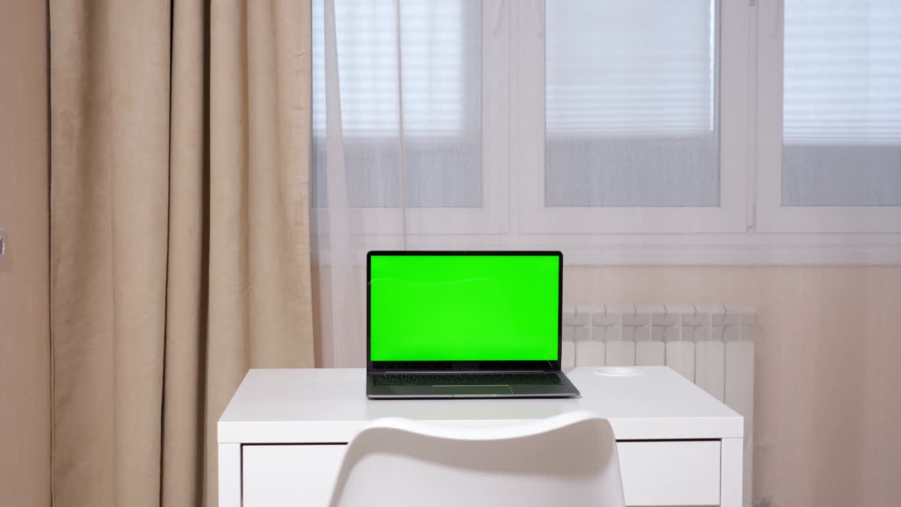 laptop with a green screen stands on a white table against the background of a window