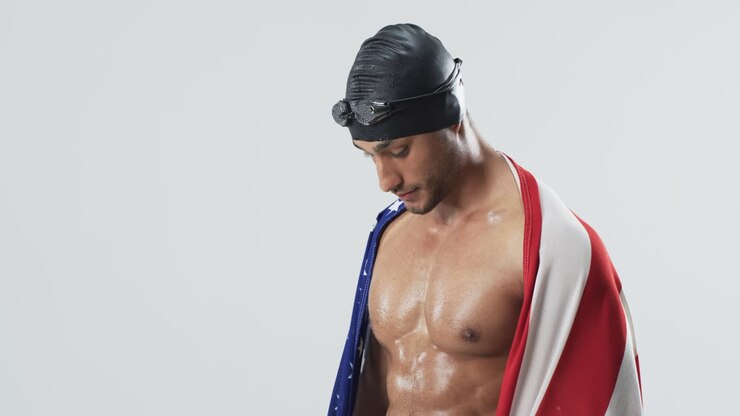 Giovane atleta nuotatore di etnia mista avvolto in una bandiera americana in uno studio fotografico.