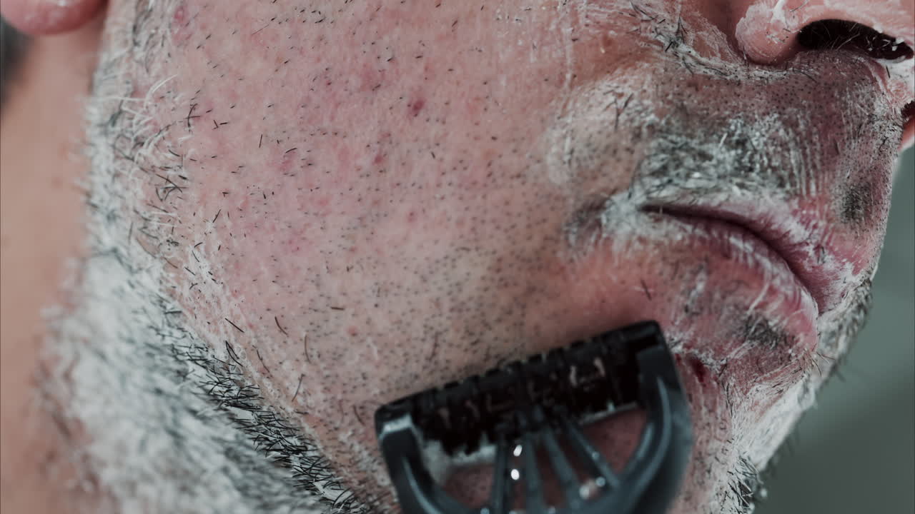 Close up of a man shaving his beard with a razor