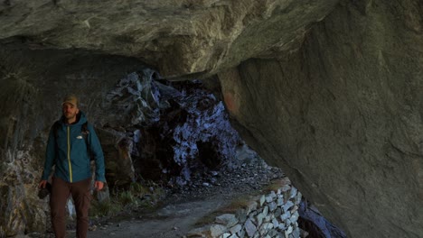 Hiker-walking-through-cave-tunnel-in-Valmalenco,-wide-shot,-handheld,-day