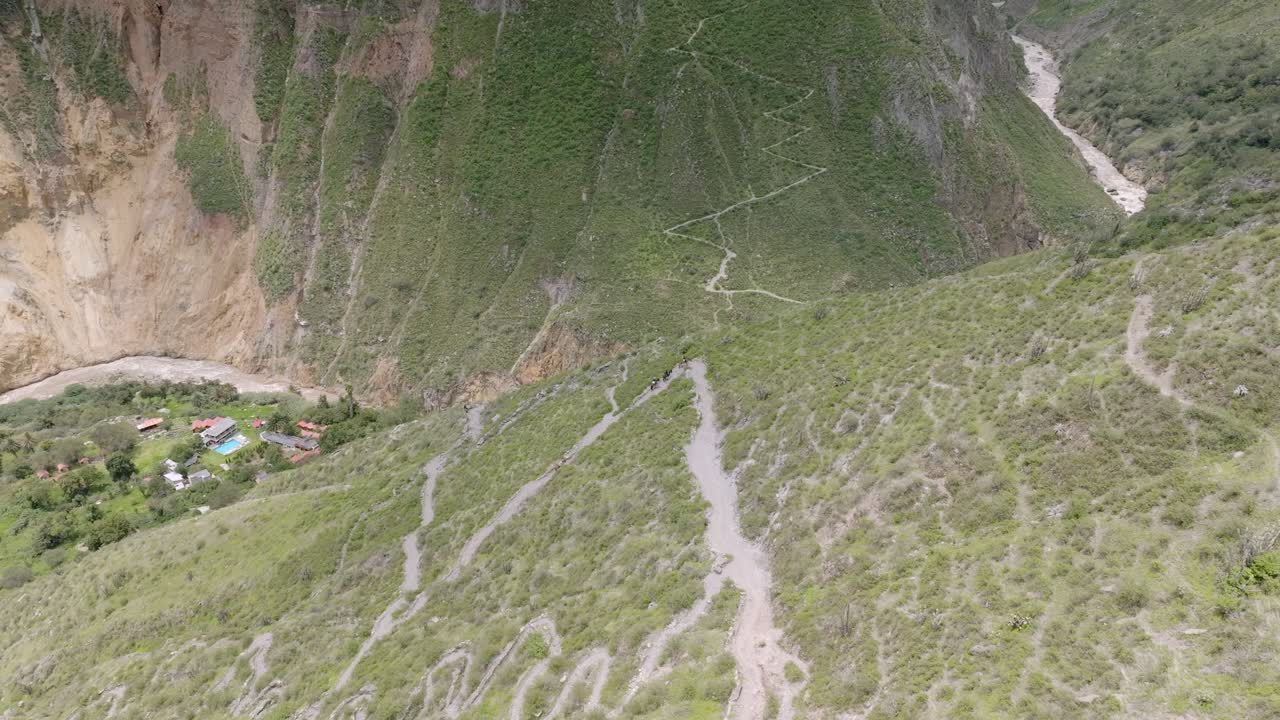 Drone shot capturing the descent along the winding path from Sangalle to Cabanaconde, with tourists riding mules, slowly making their way up through the Colca Canyon’s breathtaking landscape.
