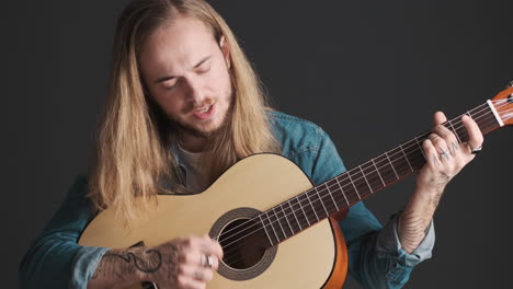 un joven caucásico tocando la guitarra y cantando ante la cámara.