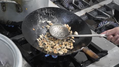 chef stir-frying mussels in a wok over a high flame in a commercial kitchen, action shot