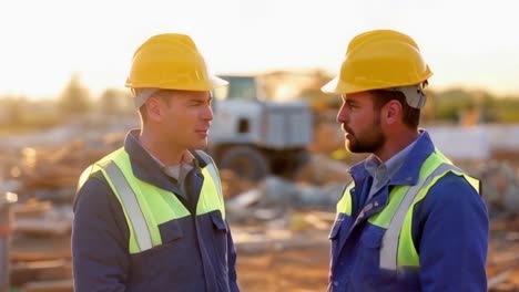 two workers in yellow helmets talking at a building construction site.