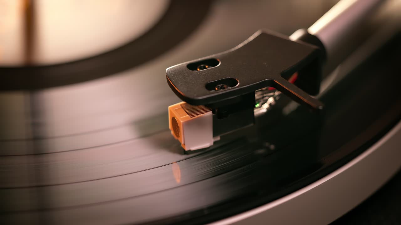 Primo piano dettagliato del braccio di un giradischi con testina bianca, posizionato su un disco in vinile nero sul piatto, che evidenzia la precisione delle apparecchiature audio