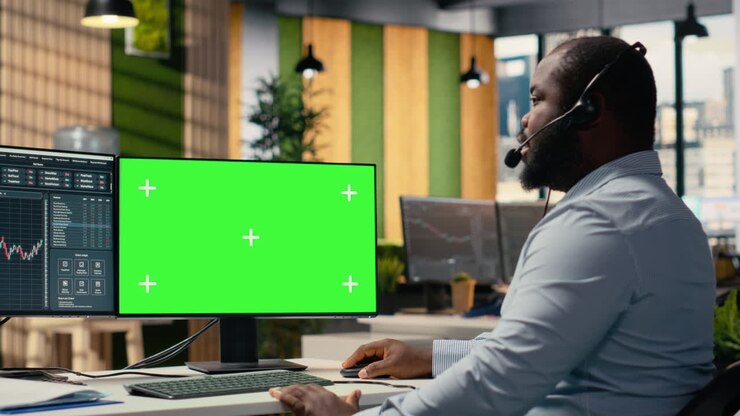 Consulente d'investimento che parla in cuffia, utilizzando un PC con schermo verde.