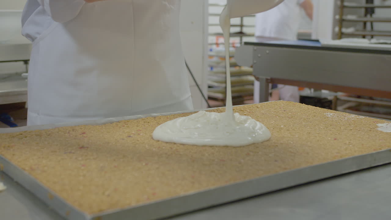 A baker pours icing mix on top of a large tray of flapjack or granola mix