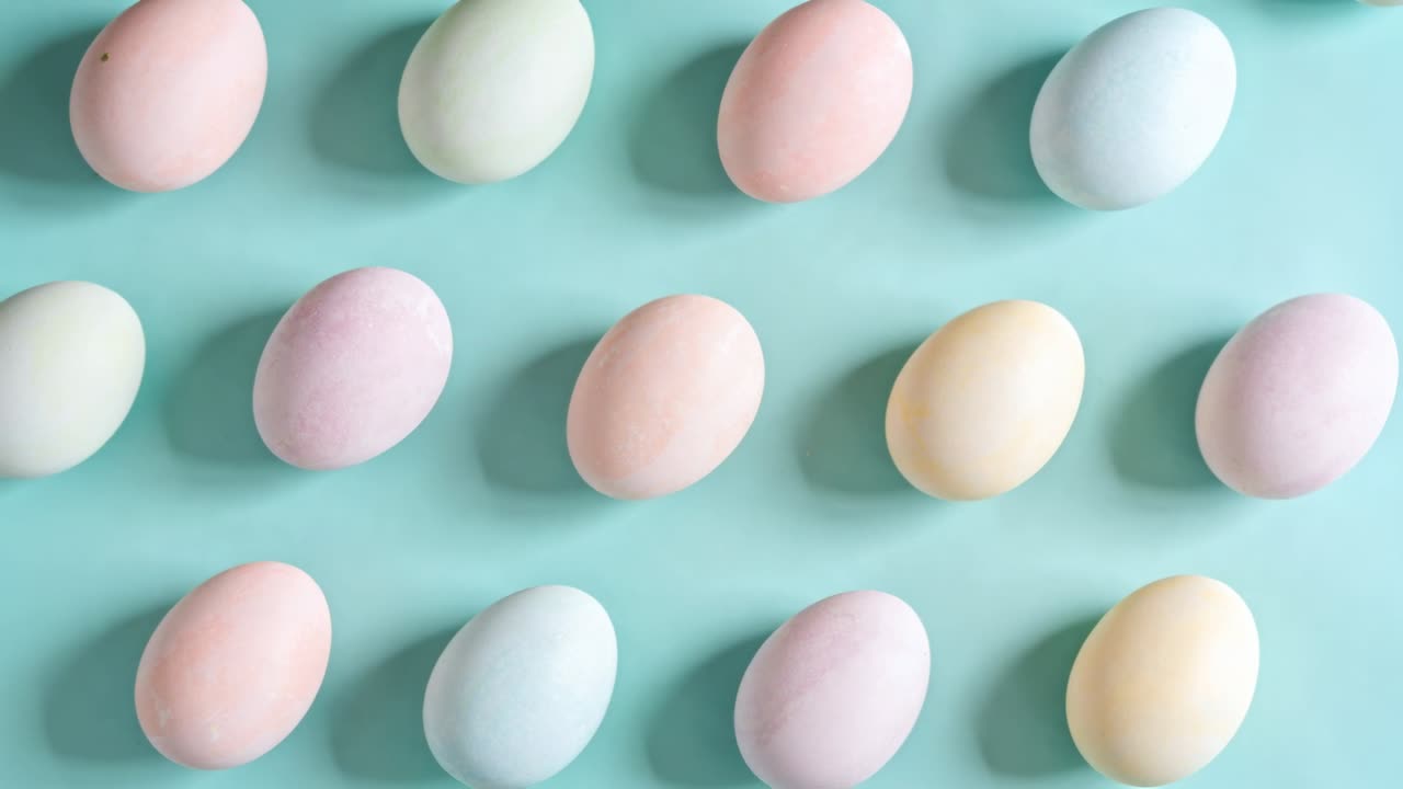 Shifting camera centering full pastel-colored egg grid on teal tabletop, revealing soft lighting