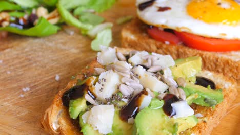 close up of homemade fried egg on a toast with sliced tomatoes and avocado toast on wooden cutting board