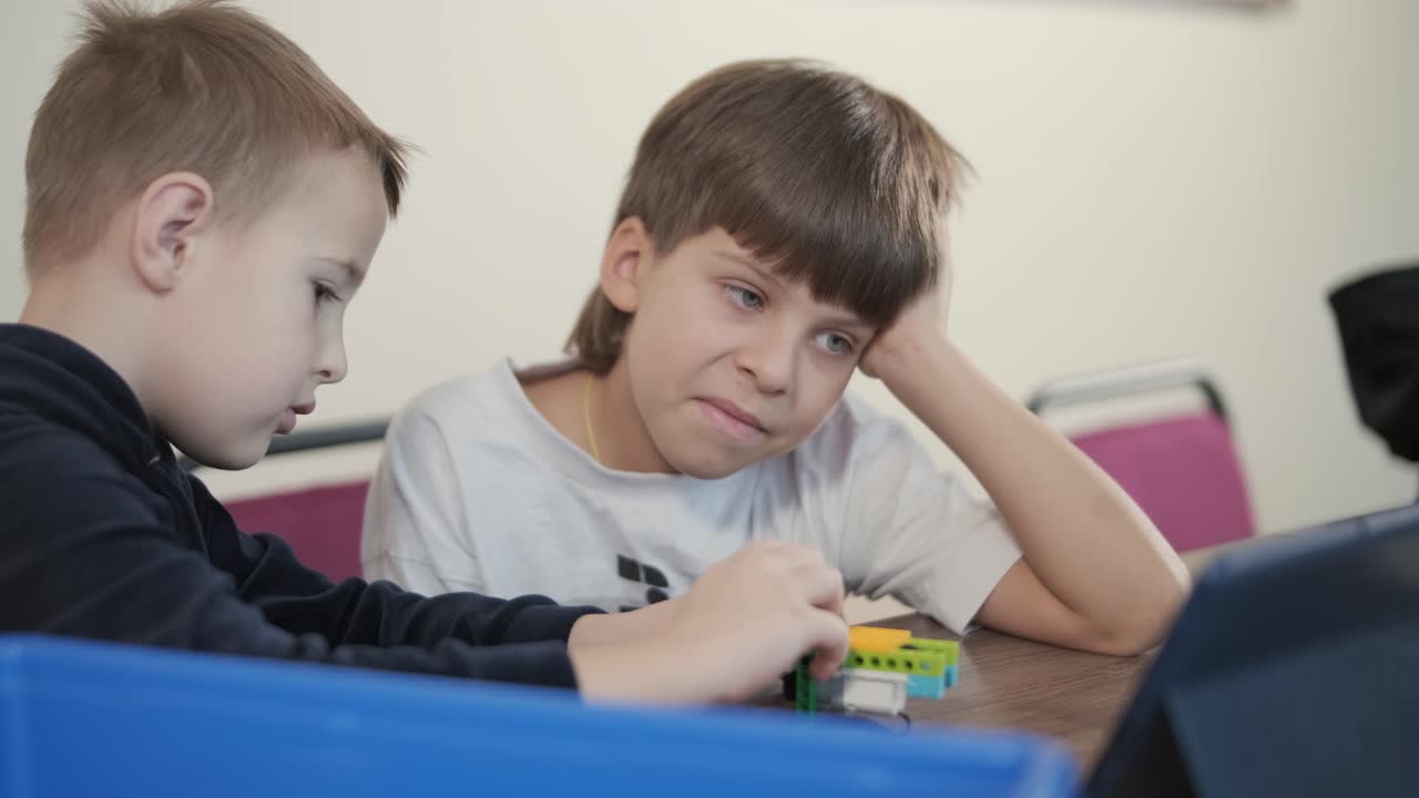Two young children intently focused on assembling parts from a robotics kit, with a tablet displaying instructions, promoting STEM learning and creativity