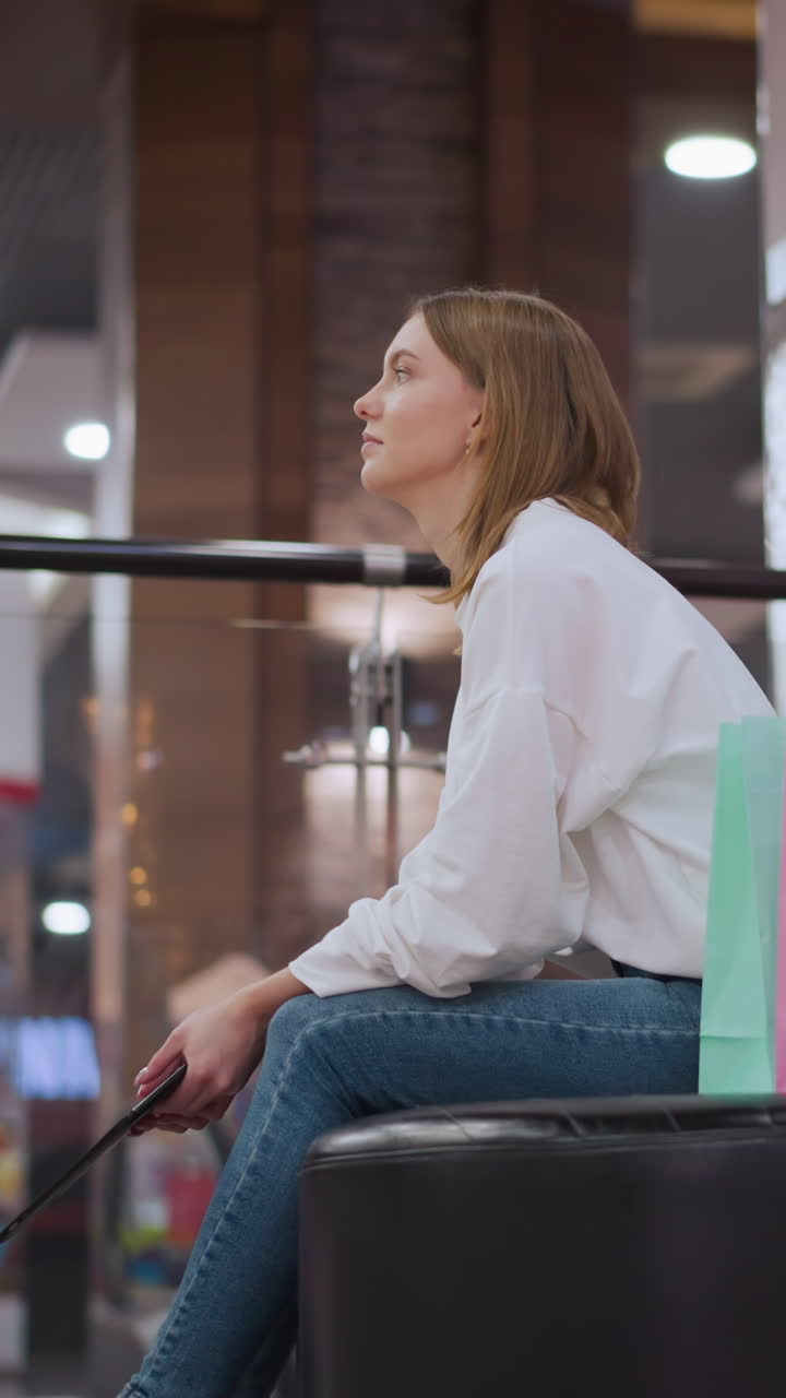 dama sentada en un banco en un centro comercial sosteniendo una tableta rodeada de decoraciones festivas, decoración de estrellas iluminadas, luces parpadeantes y bolsas de compras, con escaleras mecánicas y fondo animado