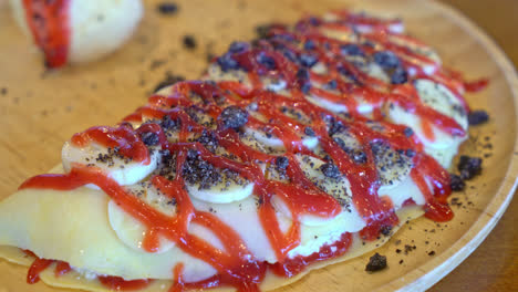 crepe-with-banana,-whipped-cream-and-strawberry-sauce-on-wood-plate