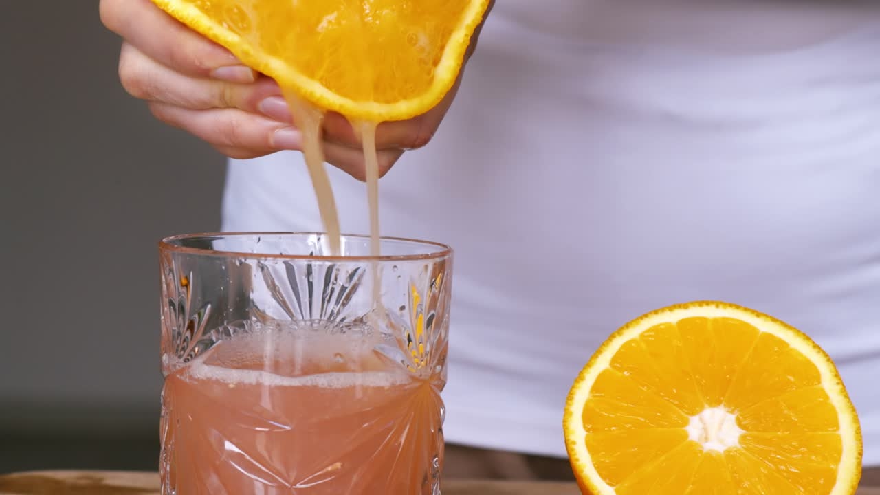 Una donna sprema il succo di un'arancia in un bicchiere. Slow motion