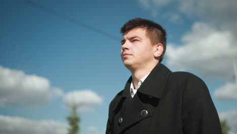 lawyer in black coat walking confidently outdoors under bright sky with sunlight reflecting off him in urban setting featuring blurred electric lines and pine tree in background