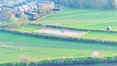 serene aerial drone shot showcasing lush green fields, residential homes, and a horse riding arena on a sunny day in wombwell, south yorkshire, england