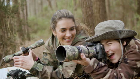 mulher feliz e seu filho observando pássaros deitados no chão da floresta