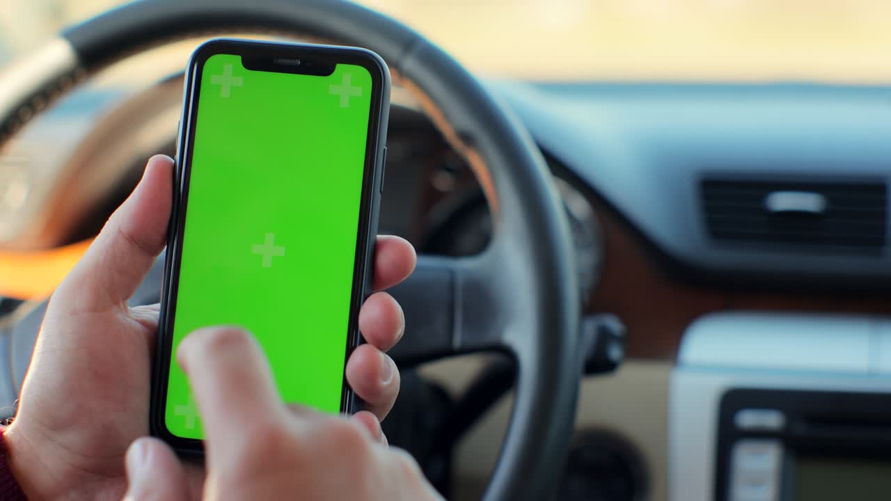 hombre sentado en un coche moderno usando un teléfono inteligente con pantalla verde clave de croma surfando por internet y tocando en la pantalla central.