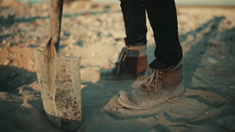 Humble-man-sticking-shovel-in-sand-in-slow-motion-at-sunset