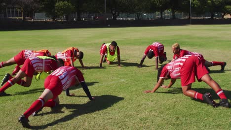 video of diverse group of male football players warming up on field,doing push-ups