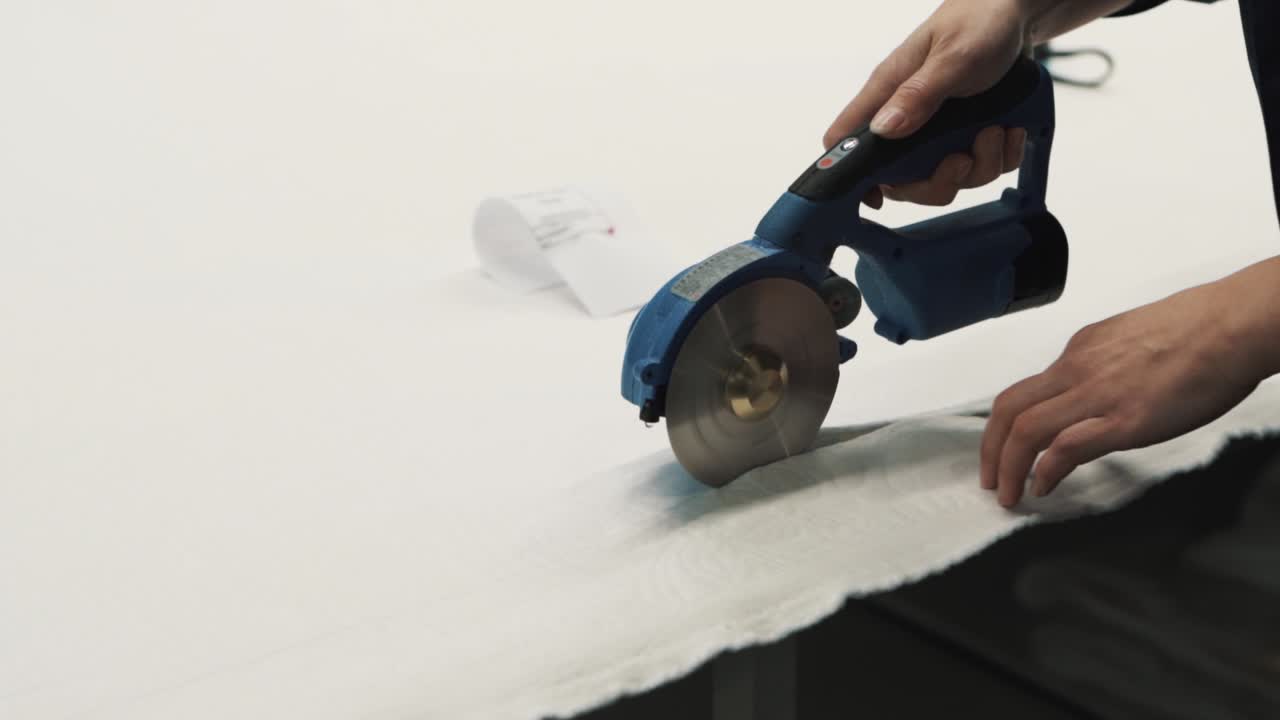 Close-up of female hands cutting white fabric with electric scissors at a textile factory