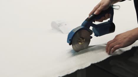 primer plano de manos femeninas cortando tela blanca con tijeras eléctricas en una fábrica textil