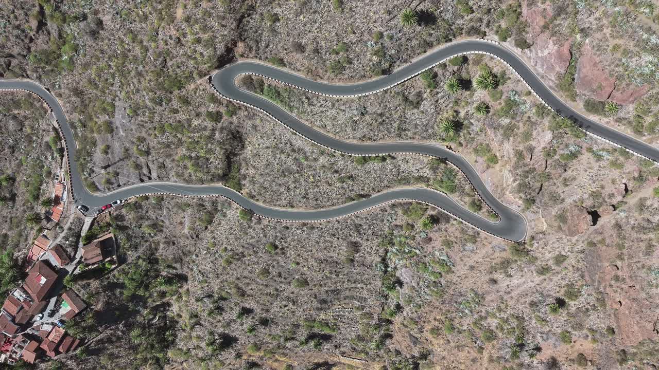Aerial view showing a narrow serpentine road and village buildings in a dry mountain