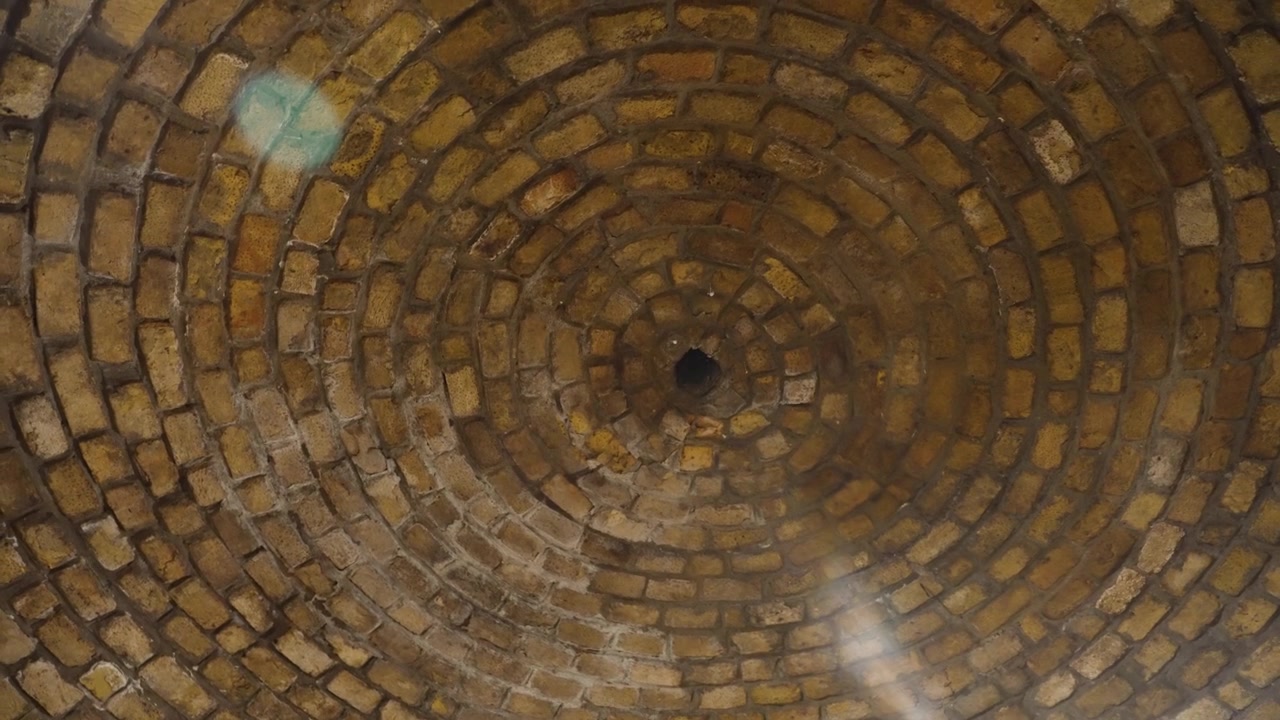 Antica cupola in mattoni in un edificio storico, illuminata da un bagliore di luce brillante che la attraversa e ruota
