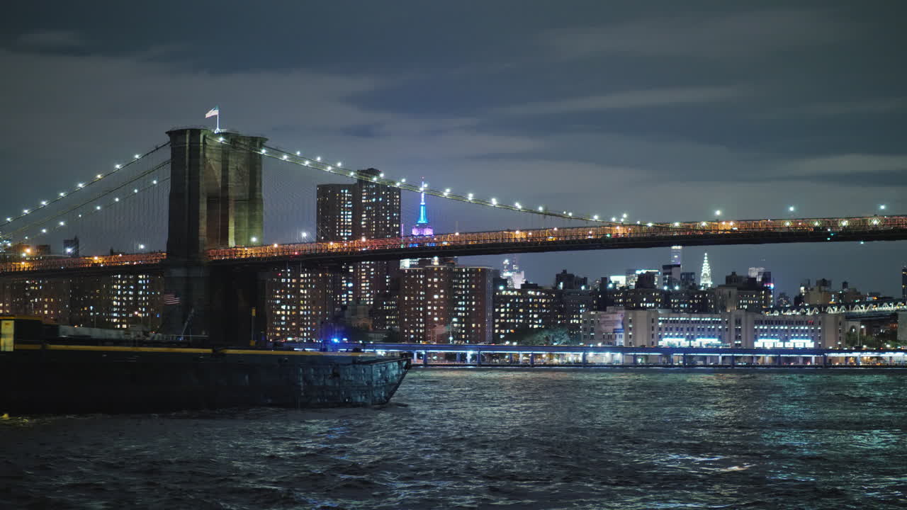 Chiatta da carico naviga sotto il Ponte di Brooklyn a New York sullo sfondo delle luci notturne di Manhattan