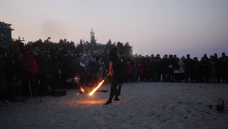 slow motion clip of a male stunt performer performing fire dances with sparking torch during fire festival on a beach in south korea.