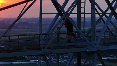 man climbing up a steel structure at sunset in preparation for a base jump, with a rural backdrop