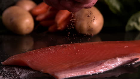 hand seasoning trout fillet in front of vegetable selection