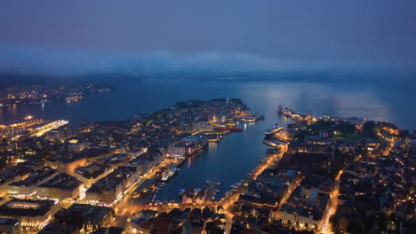 Toma-Aérea-Bajando-A-Través-De-Las-Nubes-Para-Revelar-La-Ciudad-De-Bergen,-Noruega-En-La-Noche