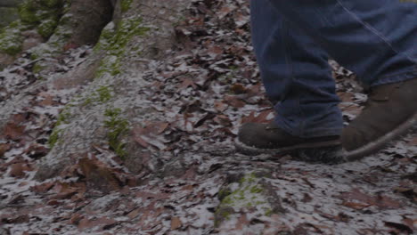 Cámara-Lenta-De-Los-Pies-De-Un-Hombre-Con-Botas-De-Montaña-Y-Jeans-Azules-Salta-Sobre-El-Suelo-Del-Bosque-Cubierto-De-Hojas-Desde-Una-Roca-Cubierta-De-Musgo-En-El-Desierto