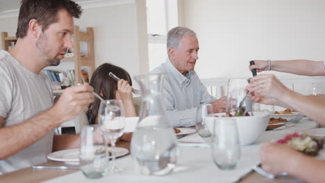 Mehrgenerationenfamilie-Sitzt-Zu-Hause-Am-Tisch-Und-Isst-Gemeinsam