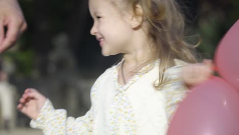 Close-up-of-the-cheerful-little-girl-playing-with-the-pink-ballons-in-the-park