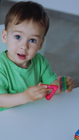 adorable toddler plays with the toys sitting at the desk. lovely baby learning colors and shapes. top view. vertical video