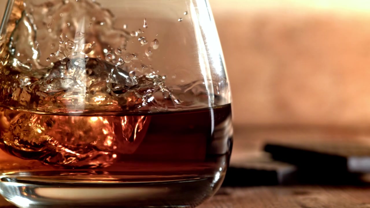 Cubo di ghiaccio che cade al rallentatore in un bicchiere di whisky