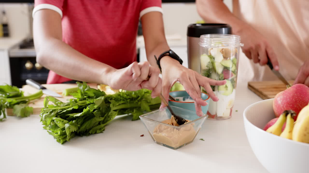 Preparing healthy smoothie, young multiracial couple adding ingredients in kitchen together, at home