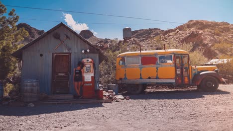 Cinemagraph---Bucle-De-Vídeo-Sin-Interrupciones-De-Una-Modelo-Joven-Parada-Junto-A-Una-Bomba-De-Combustible-De-Los-Años-50-Y-Un-Viejo-Autobús-Escolar-Amarillo-Y-Oxidado-De-Los-Años-60