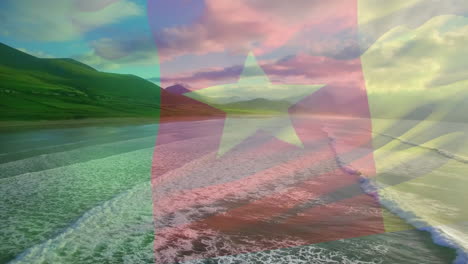 animation of flag of cameroon waving over beach landscape, cloudy blue sky and sea