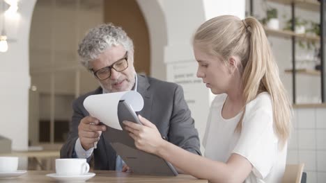 grey-haired caucasian businessman holding clipboard while blond woman signs the papers