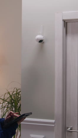 a wall-mounted security camera and a person's hands holding a smartphone