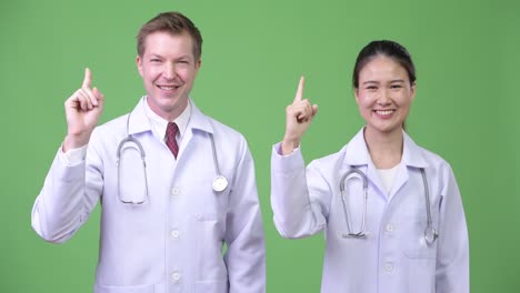 Multi-ethnic couple doctors pointing up together