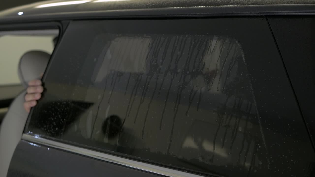 Man fitting tinting foil on side windows from the inside. Filmed from outside