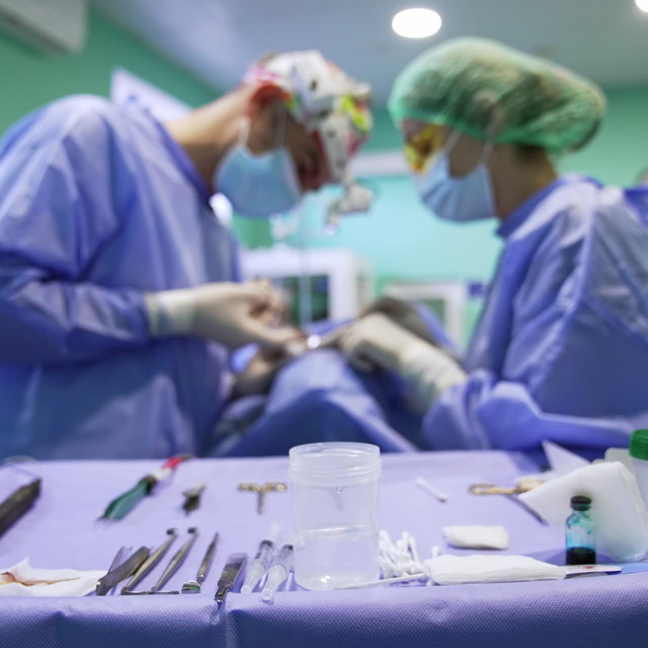 Table with tools, devices and containers in the surgery room. Doctors at backdrop perform operation in blur