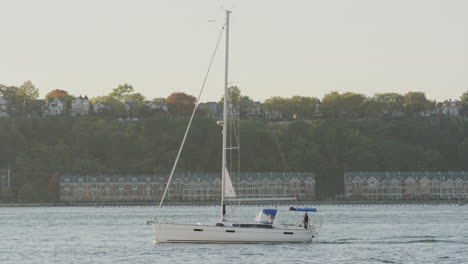 sailboat with single mast navigating along the hudson river during sunset with new jersey in the background