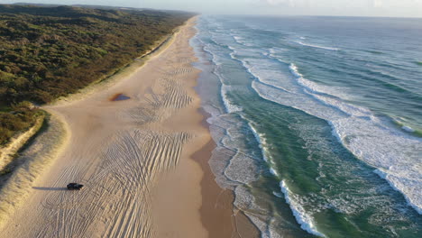 drone shot over a car on the k'gari beach, sunny morning in queensland, australia